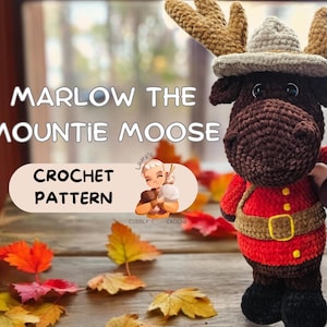 Könnte beinhalten: Ein gehäkelter Elch, der eine rot-gelbe Mountie-Uniform mit einem braunen Fellhut trägt. Der Elch steht auf einer Holzoberfläche mit Herbstblättern, die um ihn herum verstreut sind. Der Text "Marlow the Mountie Moose Crochet Pattern" ist auf dem Bild zu sehen.