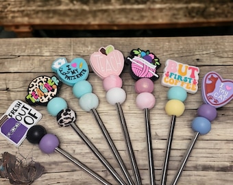 May include: Set of seven colorful stainless steel straws with various silicone toppers. Toppers include a teacher, a cat, a coffee cup, a yarn ball, an apple, a jar, and a heart.
