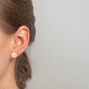 Könnte beinhalten: Nahaufnahme eines Ohrs mit einem kleinen, runden, weißen Ohrring mit strukturiertem Design.