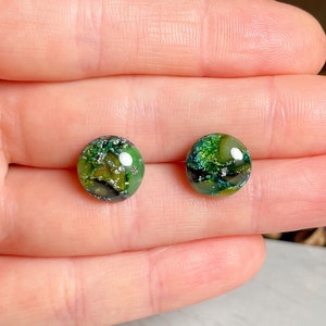 Könnte beinhalten: Ein Paar runde Glasohrringe in Grün und Schwarz mit silbernem Glitzer, der in das Glas eingebettet ist.