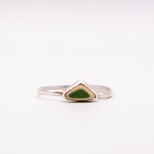 May include: A silver ring with a triangular, seafoam green and cream-colored stone. The ring is set against a white background, highlighting the minimalist design. The ring is a piece of jewelry.