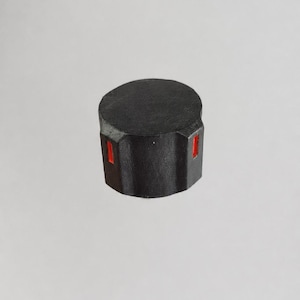 May include: A cylindrical black control knob featuring a flat top surface and a textured side profile. The side of the knob includes two small, rectangular vertical cutouts that reveal a bright orange interior accent within the black casing.