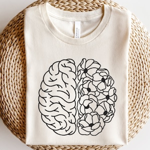 Puede incluir: Una camiseta blanca con un dibujo en línea negra de un cerebro con flores en un lado.