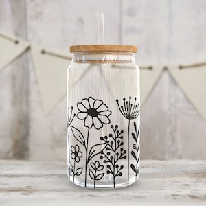 May include: A clear glass jar with a wooden lid and a black and white floral design. The jar has a straw sticking out of the lid.
