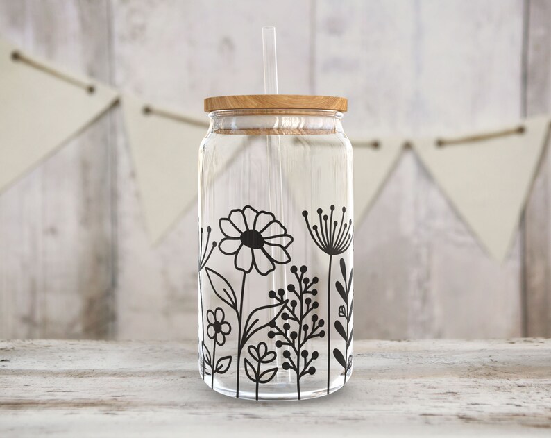 May include: A clear glass jar with a wooden lid and a black and white floral design. The jar has a straw sticking out of the lid.