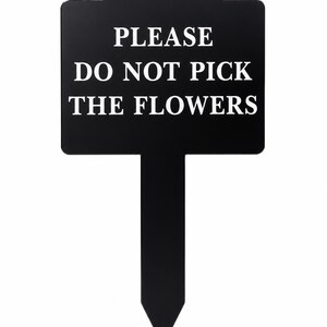 May include: A black garden sign with a rectangular top and a pointed stake base. The sign features white text that reads PLEASE DO NOT PICK THE FLOWERS in a serif font. The sign has a smooth finish and a curved top edge for a clean appearance.