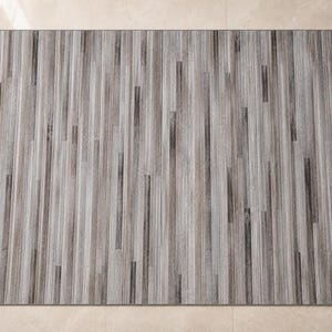 May include: A rectangular area rug featuring a vertical striped pattern in shades of gray, charcoal, and white. The design consists of varying widths of linear bands that create a textured appearance across the entire surface of the floor covering.