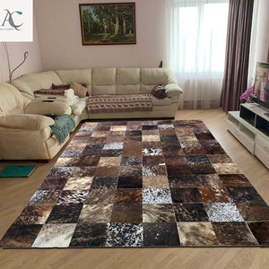 May include: A large, rectangular rug with a patchwork design. The rug features squares of varying shades of brown, beige, and white, creating a textured, natural look. The rug is placed on a wooden floor in a living room setting.