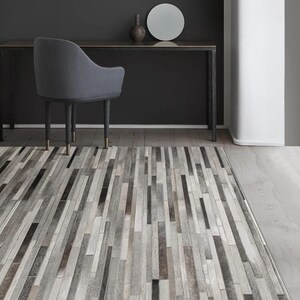 May include: A rectangular area rug featuring a patchwork design of vertical strips in varying shades of gray, charcoal, white, and silver. The rug is composed of narrow, elongated rectangular segments arranged in a linear, repeating pattern.