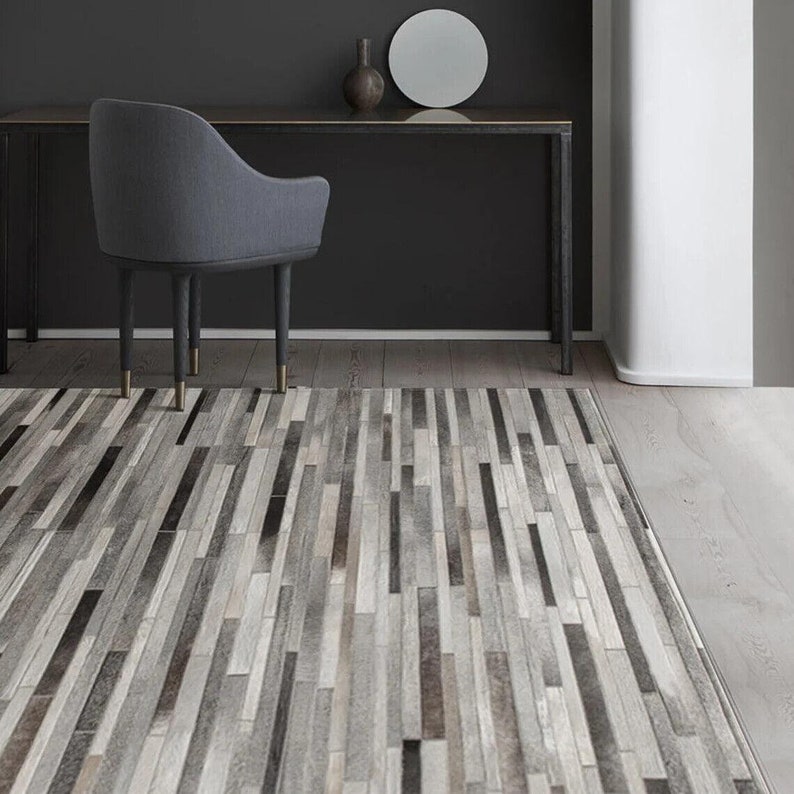 May include: A rectangular area rug featuring a patchwork design of vertical strips in varying shades of gray, charcoal, white, and silver. The rug is composed of narrow, elongated rectangular segments arranged in a linear, repeating pattern.
