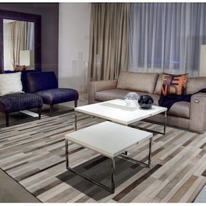 May include: A living room set featuring a beige sofa with a dark throw, two purple textured armchairs, and two square white coffee tables with chrome frames. A large rectangular area rug with a striped pattern in shades of brown, gray, and white.