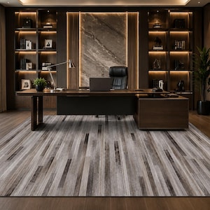 May include: A rectangular area rug featuring a vertical striped pattern in shades of gray, charcoal, and white, mimicking the appearance of weathered wood planks. The rug is positioned on a dark wood floor in a home office with a desk and shelving.