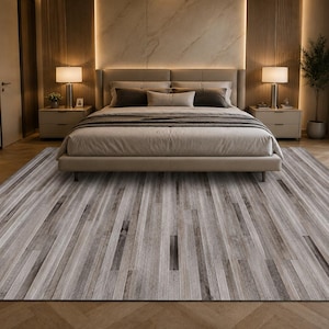 May include: A large rectangular area rug featuring a pattern of vertical stripes in varying shades of gray, white, and brown, mimicking the appearance of weathered wood planks. The rug is positioned on a light-colored herringbone wood floor.