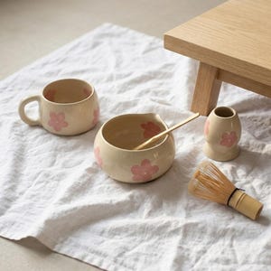 Pu&ograve; includere: Un set da matcha in ceramica composto da una tazza color crema, una ciotola con beccuccio e un supporto per frusta, tutti decorati con motivi floreali rosa. Una frusta in bamb&ugrave; e un cucchiaio in bamb&ugrave; completano questo set per il t&egrave;.