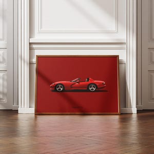 Puede incluir: Impresión enmarcada de un coche deportivo rojo, sobre un fondo rojo. El coche es un descapotable con ruedas plateadas. El marco es de color marrón cálido y la impresión se muestra sobre un suelo de madera.