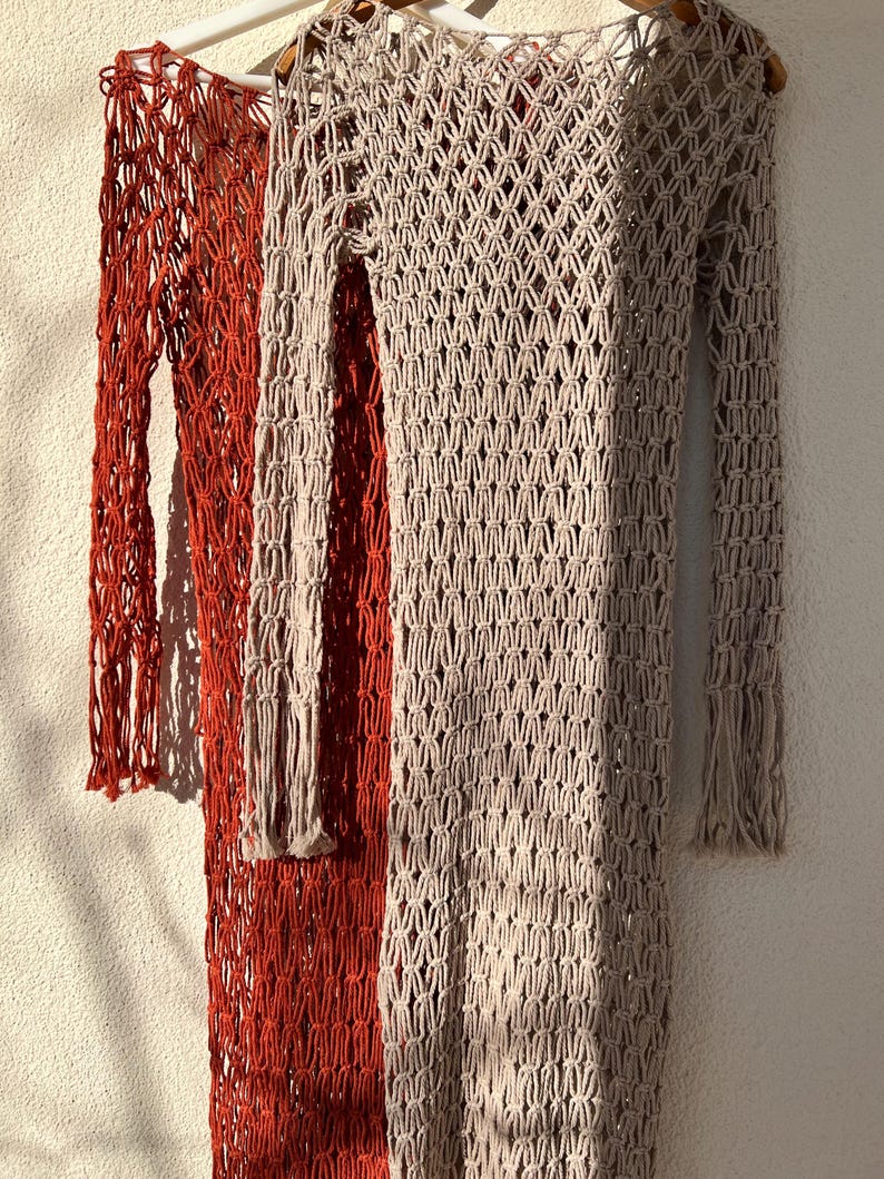 May include: Two crocheted dresses, one in a rust orange color and the other in a light beige color. Both dresses have a long-sleeved, loose-fitting style with a delicate, open-weave pattern.