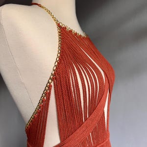 May include: A rust-colored halter top made of crocheted yarn with a gold chain detail.