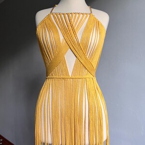 May include: A yellow macrame halter top with a fringe bottom. The top is made of a thick cord and has a criss-cross design in the front.
