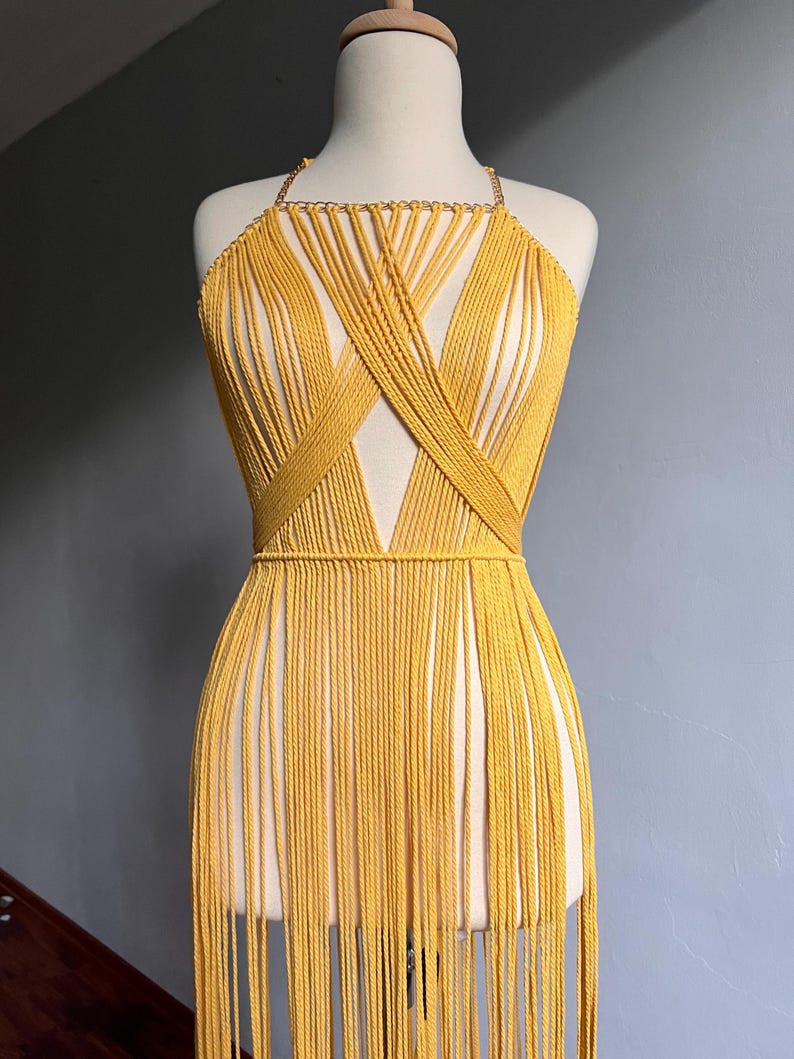 May include: A yellow macrame halter top with a fringe bottom. The top is made of a thick cord and has a criss-cross design in the front.