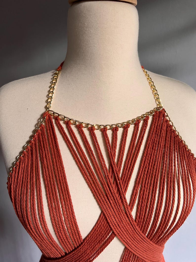 May include: A red crocheted halter top with a gold chain detail. The top is made of many thin strands of yarn that are woven together to create a criss-cross pattern.