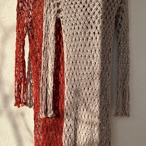 May include: Two crocheted dresses, one in a rust orange color and the other in a light beige color. Both dresses have a long-sleeved, loose-fitting style with a delicate, open-weave pattern.