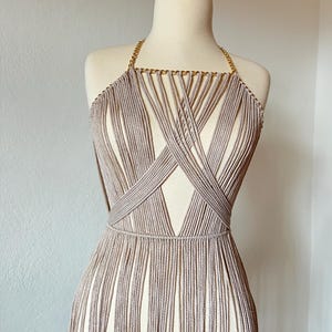 May include: A beige crocheted top with a gold chain detail and fringe. The top is on a white mannequin.