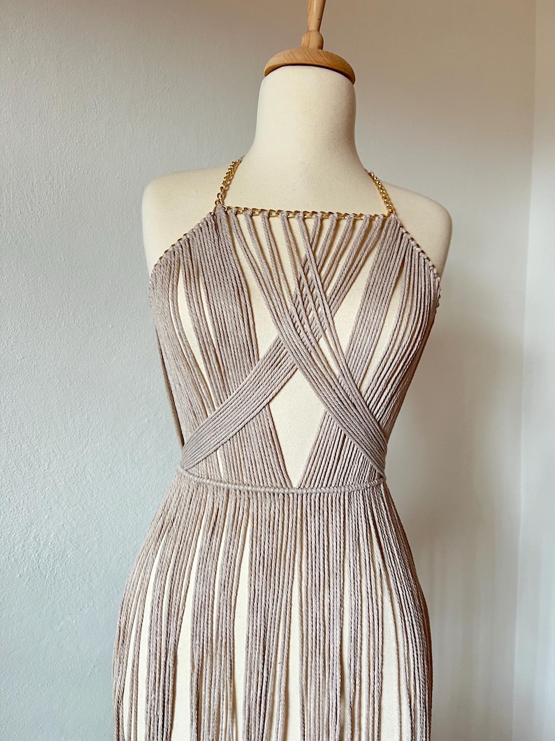 May include: A beige crocheted top with a gold chain detail and fringe. The top is on a white mannequin.