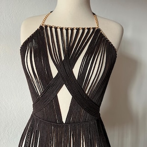 May include: A brown crocheted halter top with a gold chain detail. The top has a fringe hem and a criss-cross design in the front.