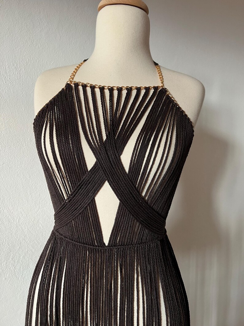 May include: A brown crocheted halter top with a gold chain detail. The top has a fringe hem and a criss-cross design in the front.