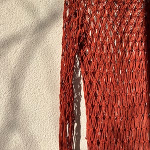 May include: A rust-colored crochet top with long sleeves and a loose fit. The top is made of a thick, textured yarn and has a delicate, open-weave design.