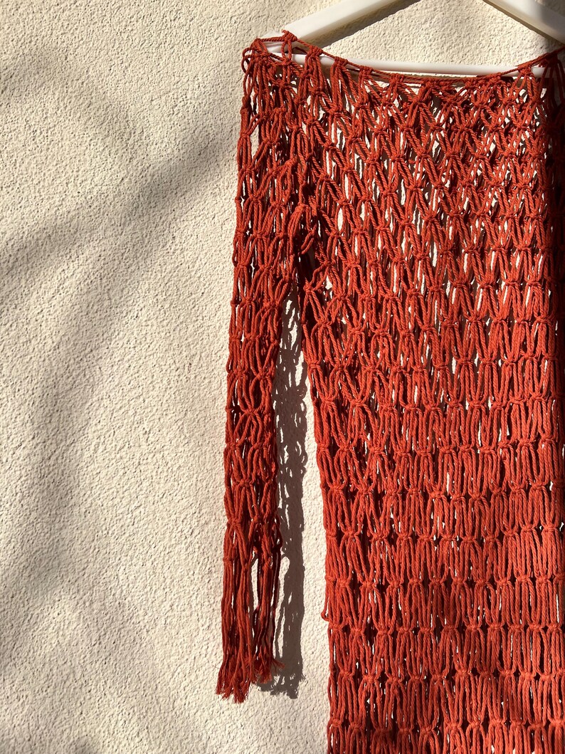 May include: A rust-colored crochet top with long sleeves and a loose fit. The top is made of a thick, textured yarn and has a delicate, open-weave design.
