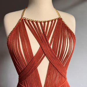 May include: A rust-colored crocheted top with a gold chain detail. The top has a deep V-neckline and a fringe hem.