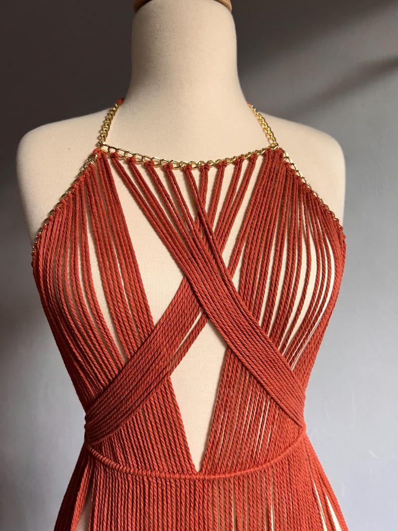 May include: A rust-colored crocheted top with a gold chain detail. The top has a deep V-neckline and a fringe hem.