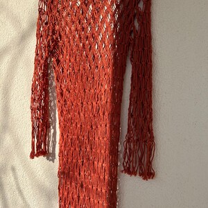 May include: A rust-colored crochet dress with long sleeves and a loose fit. The dress is made of a fine, open-weave material.