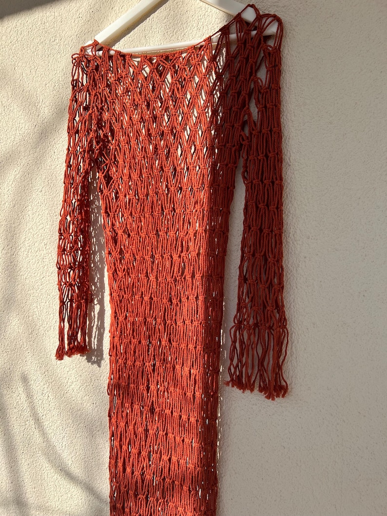 May include: A rust-colored crochet dress with long sleeves and a loose fit. The dress is made of a fine, open-weave material.