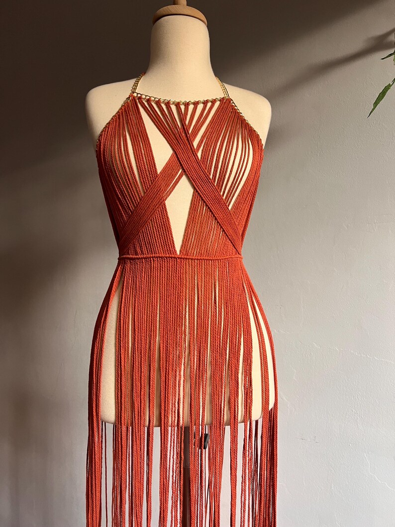 May include: A burnt orange halter top with a gold chain detail and a fringe bottom.
