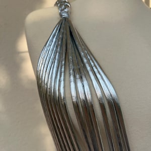 May include: A silver dress with a unique strap design. The strap is made of multiple thin, metallic strips that cascade down the shoulder. The dress is displayed on a mannequin, showcasing the intricate details and texture of the fabric.