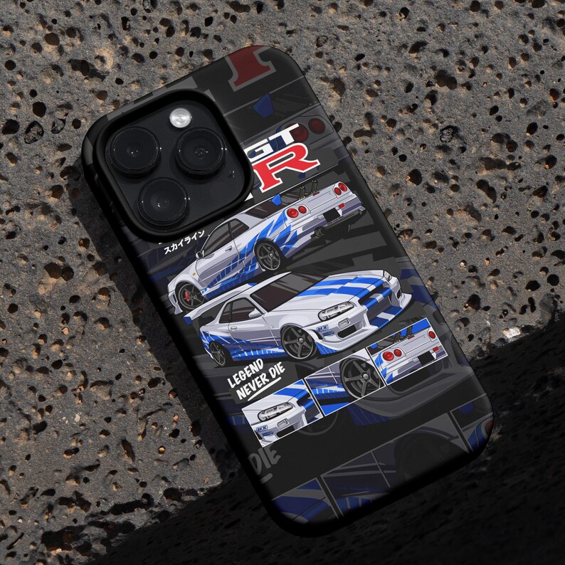 Pu&ograve; includere: Una custodia per iPhone nera con una grafica bianca e blu di una Nissan Skyline GT-R. La custodia presenta il testo "LEGEND NEVER DIE" e "GT-R" in bianco.