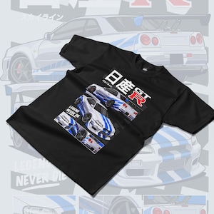 Pu&ograve; includere: Maglietta nera con una grafica bianca e blu di una Nissan Skyline GT-R. La grafica include il testo "LEGEND NEVER DIE" e "日産 GT-R".