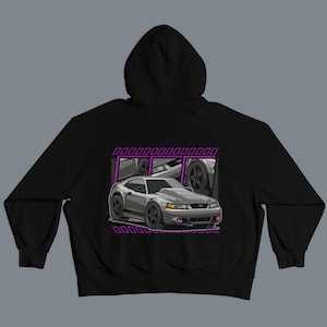 May include: Black hooded sweatshirt featuring a graphic of a gray sports car with purple accents. The car illustration is set against a purple rectangular frame. The design includes details of the car's wheels and headlights.