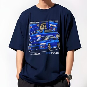 Pu&ograve; includere: Una t-shirt blu navy con una grafica di una Subaru Impreza WRX blu. La grafica presenta pi&ugrave; angolazioni dell'auto e il testo "SUBARU" e "AWD POWER".