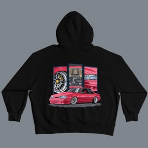 May include: Black hooded sweatshirt featuring a red car graphic. The graphic shows a detailed illustration of a red car with three inset panels displaying car parts. The car has silver rims and a low profile.