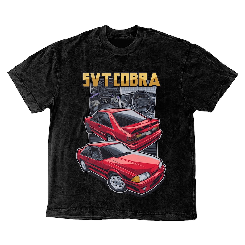 May include: Black t-shirt featuring a graphic of two red SVT Cobra cars. The cars are depicted in a stylized illustration with a gold "SVT COBRA" text at the top. The t-shirt has a vintage, acid wash appearance.