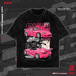 May include: Black t-shirt featuring a pink Honda S2000 car illustration. The design includes the text "SUKI" and "Veil Side", along with Japanese characters and the phrase "JDM Car Illustration". The shirt has a crew neck.