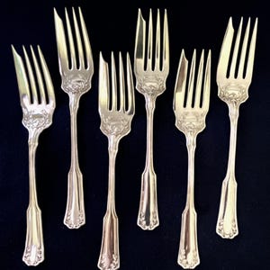 May include: Set of six silver cake forks with ornate handles. The forks have a vintage look and are in good condition.
