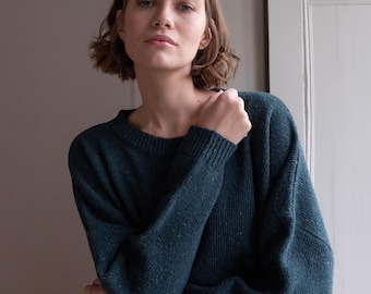 May include: A teal-colored sweater with a crew neck and long sleeves. The sweater has a speckled texture and is worn by a person. The person is looking at the camera.