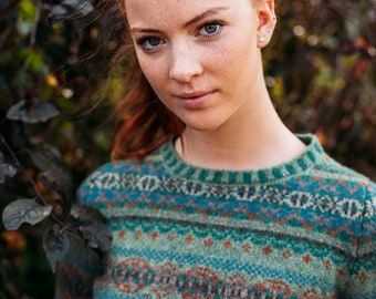 Può includere: Una donna con i capelli rossi indossa un maglione a motivi verdi, blu e rossi. Il maglione ha un design a Fair Isle.