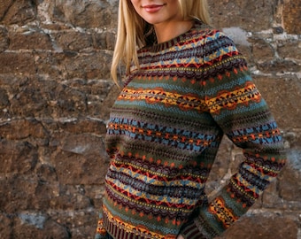 Può includere: Un maglione a maniche lunghe con un motivo geometrico colorato in tonalità di verde, marrone, rosso, blu e giallo. Il maglione ha un collo rotondo e una vestibilità comoda.