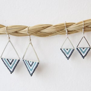 May include: Three pairs of silver triangle earrings with geometric patterns in shades of blue, white and black.
