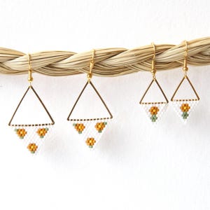 May include: A pair of gold triangle earrings with white and orange beaded flowers hanging from them.